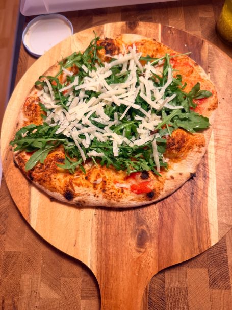 Pizza mit Tomatensauce, Hühnchen, Rucola und geriebenem Käse auf einem Holzbrett.